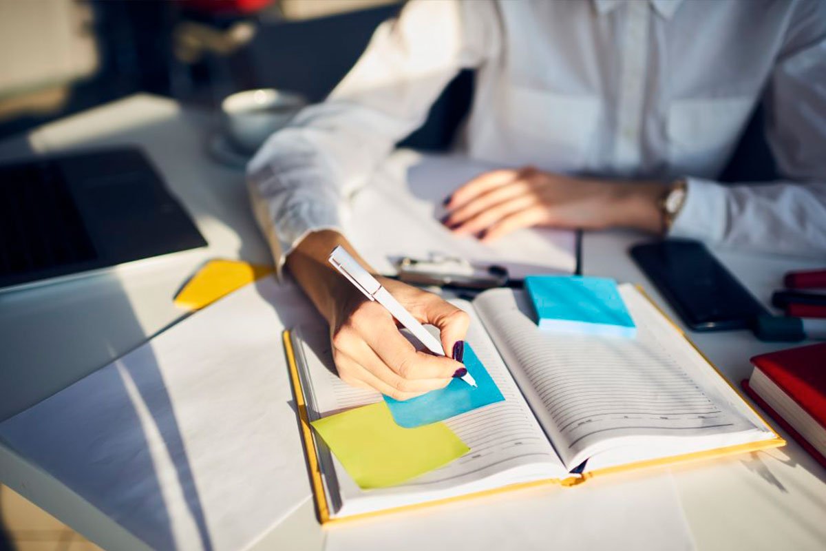 pessoa sentada em sua mesa de trabalho escrevendo em seu caderno