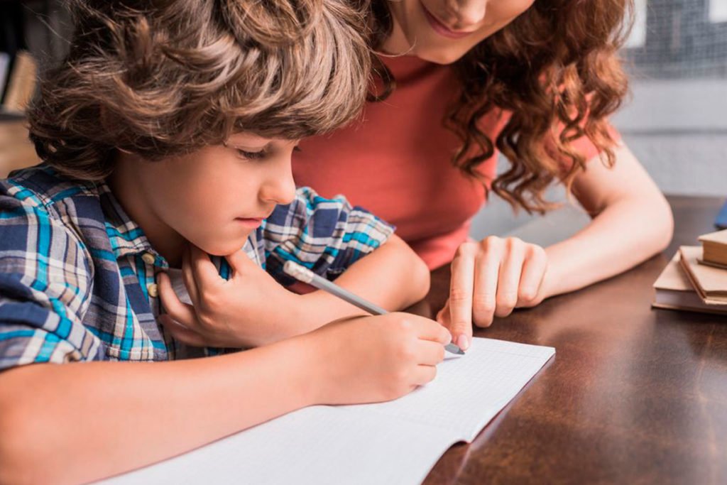 criança escrevendo em um caderno e uma mulher o auxiliando