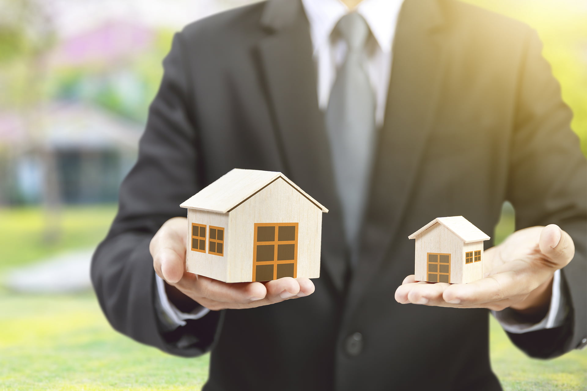 homem de terno segurando duas casas em miniatura